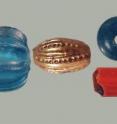 In the top left is a common cobalt blue seed bead, most likely from Venice (20,906 found). Below that is a Venetian turquoise/green-blue seed bead or <i>rocaille</i> (5777 found). To the right of these is a unique blue green melon bead from China, then a Spanish gilded oval glass bead (15 found). On the top right is an Ichtucknee plain turquoise blue bead with white patinas now thought to be manufactured in France (one of 5,265).  Below that is a green Heart bugle bead with a thin clear veneer over red-orange glass over green glass from the <i>Margariteri</i> guild of Venice (one of 5).