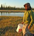 University of Utah biologist Mike Shapiro, with mosquito netting for protection, walks along one of the Fox Holes Lakes in Canada's Northwest Territories. Shapiro collects stickleback fish from this and other lakes and the ocean for studies of the genetics of diversity in the animal world, and how identical traits in different species can arise sometimes from the same gene, and sometimes from different genes.