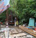 This photo shows colleague Chiching Liu with the drill rig and the strainmeter on the ground front left. The small blue enclosure to the right houses the electronics. The picture was taken shortly before the installation of the strainmeter.