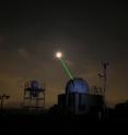NASA Goddard's Laser Ranging Facility directing a laser (green beam) toward the LRO spacecraft in orbit around the moon (white disk). The moon has been deliberately over-exposed to show the laser.