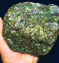 This is an image of a sample of cratonic mantle root from Kimberley, South Africa. The rock consists of dark green olivine, whitish-green enstatite, emerald green diopside and purple garnet.