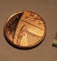 This is the photonic chip next to a UK penny. The chip contains micrometer and sub-micrometer features and guide light using a network of waveguides. The output of this network can be seen on the surface of the chip.