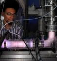 Ph.D. student Gilles Adande monitors the reaction chamber in which the methane-metal hybrid molecule is produced. Ionized gas inside the chamber emits a pink glow.