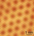 Under the scanning tunneling microscope, graphene reveals its honeycomb structure made up of rings of carbon atom, visible as small hexagons. The larger hexagons result from an interference process occurring between the graphene and the underlying boron nitride. The scale bar measures one nanometer, or one billionth of a meter.