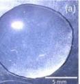 Figure (a) shows a roughly circular water droplet containing silica nanoparticles resting on an untreated glass surface. Figure (c) demonstrates how a UV laser can alter the surface texture, allowing the droplet to preferentially flow over the more wettable section, changing the shape of the droplet.