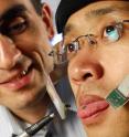 Georgia Tech assistant professor Maysam Ghovanloo (left) points to a small magnet attached to graduate student Xueliang Huo's tongue that allows him to operate a computer mouse and powered wheelchair.