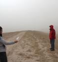 During a windstorm on China's Loess Plateau, geoscientist Fulong Cai uses a plastic bag as a wind sock to show that the wind blows parallel to the linear ridge he and Wang Zhao are standing on. Roads in this area run along the ridges.