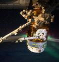 The Japan Aerospace Exploration Agency (JAXA) Kounotori H-II Transfer Vehicle (HTV-5) is seen berthed to the International Space Station. The external CALET experiment, which will search for signatures of dark matter, is seen being extracted from the unpressurized section by the station's robotic arm, Canadarm2. An aurora over the Earth limb is visible in the background.