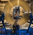 Sandia National Laboratories technician Eric Breden installs a transmission cable on the silver disk that is the new pulsed-power machine's central powerflow assembly. (Photo by Randy Montoya). Click on the thumbnail for a high-resolution image.