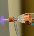 The nozzle firing a jet of carbon nanotubes with helium plasma off and on. When the plasma is off, the density of carbon nanotubes is small. The plasma focuses the nanotubes onto the substrate with high density and good adhesion.