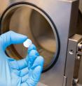 The sample makes a steel substrate look blue. Behind the hand is a ALD reactor.