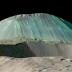 Volcanic dome Ahuna Mons rises above a foreground impact crater, as seen by NASA's Dawn spacecraft with no vertical exaggeration. Eruptions of salty, muddy water built the mountain by repeated eruptions, flows, and freezing. Streaks from falls of rocks and debris run down its flanks, while overhead views show fracturing across its summit.